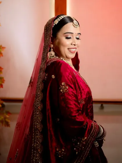 A side profile of my bride in her deep red velvet lehenga. The soft lighting highlights the glowing skin and the gentle contour of her makeup.