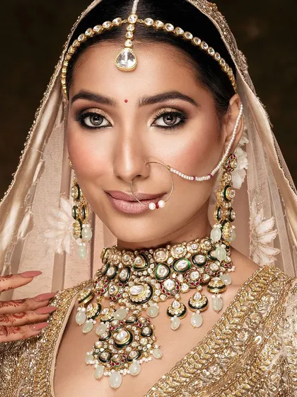 A quintessential bridal beauty shot, capturing a serene expression and the stunning details of the gold jewelry and makeup.