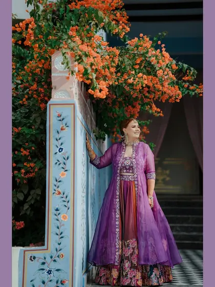 A stunning portrait of the bride Joleen in her vibrant purple Mehendi outfit, set against a colorful, hand-painted Rajasthani wall.