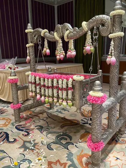 A beautifully decorated silver cradle for a naming ceremony. The cradle is adorned with garlands of jasmine, pink roses, and lotus buds, showcasing my attention to detail.