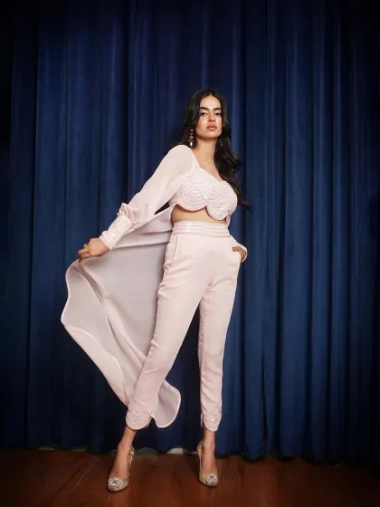 A full-length shot of a beautiful pastel pink co-ord set with a flowing cape. The pose is dynamic, showing the movement of the fabric against a rich blue backdrop.