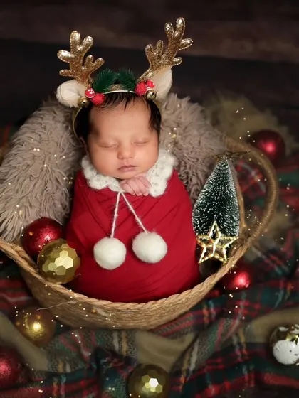 A little reindeer fast asleep. This Christmas-themed newborn portrait is full of festive cheer, with plaid blankets and shiny ornaments.