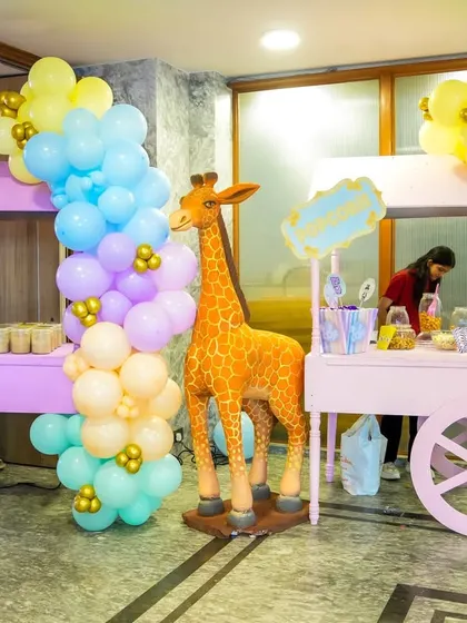 A pair of pastel pink food carts serving cotton candy and other treats, flanked by a tall giraffe prop at a carnival party.