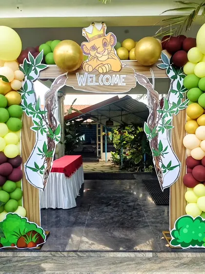A grand entrance arch for a jungle party. The balloon arch in earthy tones is decorated with faux vines and a 'Welcome' sign featuring Simba from The Lion King, setting the tone from the moment guests arrive.