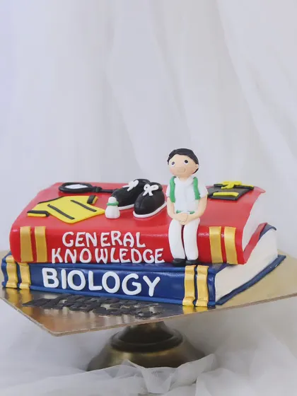 For the book lover, this cake is shaped like a stack of textbooks. The design features "General Knowledge" and "Biology" books, topped with fondant sports equipment for a student who loves to learn and play.