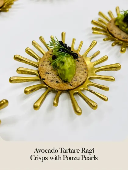 An elegant presentation of our Avocado Tartare on a Ragi Crisp, topped with ponzu pearls and served on a sunburst-shaped brass plate.