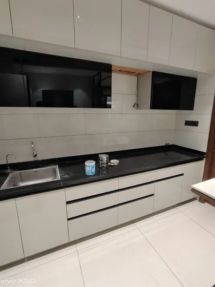A simple and sleek parallel kitchen with white handleless cabinets and a black countertop. The black glass accent on the upper cabinets adds a touch of modern contrast.