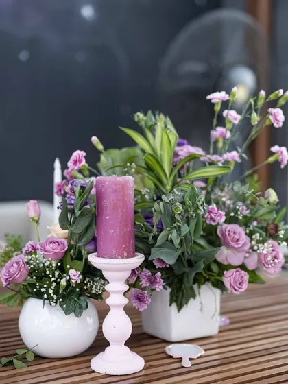 A table centerpiece detail, with a pastel purple candle holder and a mix of fresh flowers in shades of lavender and pink.