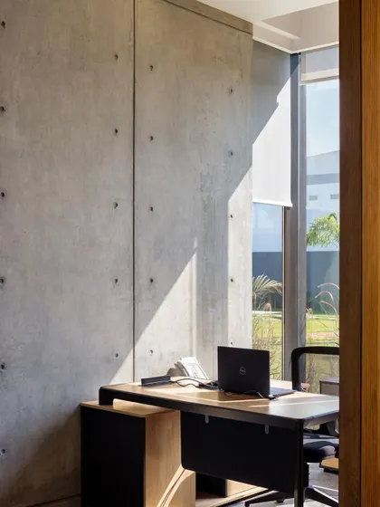 A private office cabin featuring a board-formed concrete wall. The raw texture of the concrete is softened by the abundant natural light from the large window.