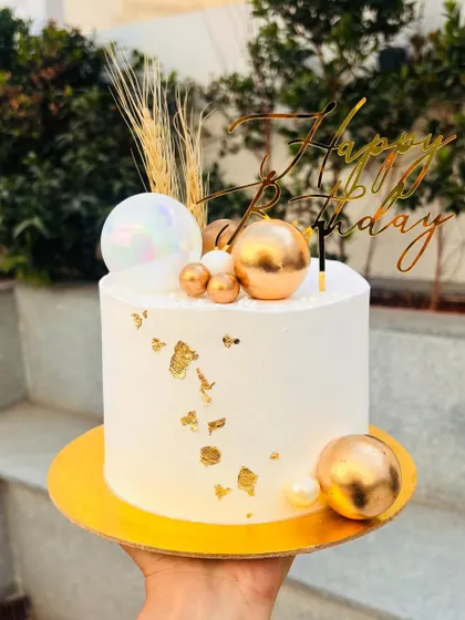 Beauty in white and gold. This elegant cake is decorated with gold spheres, gold leaf, and dried wheat stalks for a rustic yet chic look.