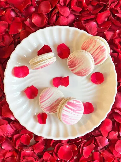 A plate of my Rose Water Macarons, resting on a bed of fresh rose petals. The marbled pink and white shells are so pretty, and the flavor is a delicate expression of devotion, perfect for the festive season.