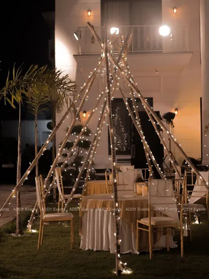 A closer look at our fairy-lit teepee dining setup against the backdrop of a modern farmhouse. This arrangement is perfect for creating intimate and cozy dining pods within a larger outdoor event space.
