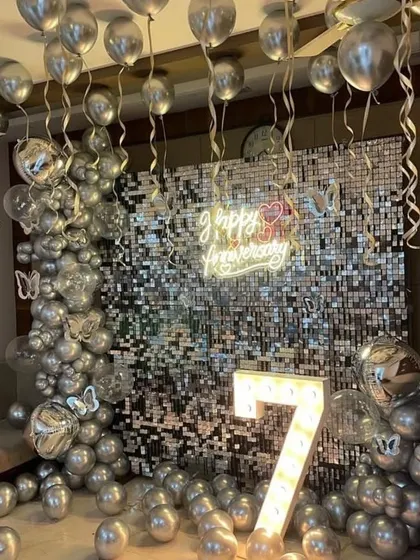 A dazzling 7th-anniversary party with a silver sequin wall, a silver balloon arch, and a light-up number '7'.
