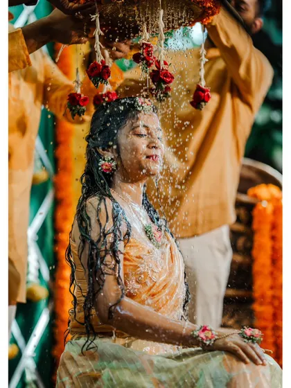 A beautiful and dramatic shot of a bride being showered with water and red rose petals during her Haldi.