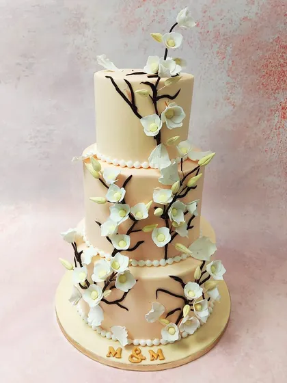 We create a breathtaking centerpiece with this three-tiered cherry blossom wedding cake. Delicate, handcrafted sugar cherry blossoms gracefully climb dark branches against a soft blush-colored fondant, embodying the beauty and elegance of a spring wedding.