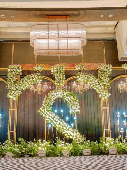 A direct, symmetrical view of the floral "S" stage design. This shot highlights the balance and precision in our decor, with chandeliers and lighting perfectly framing the central motif under a grand ballroom chandelier.