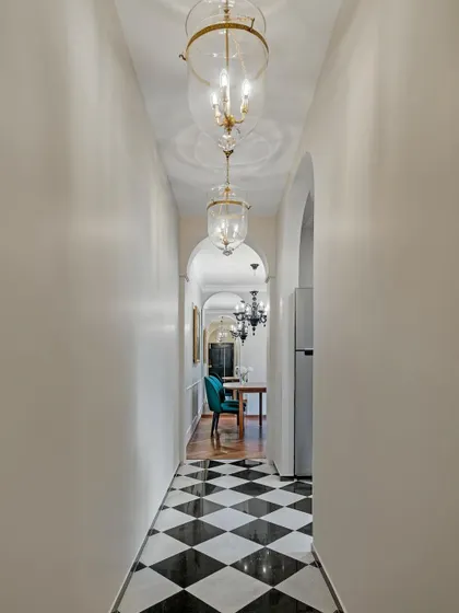 This hallway in a modern Victorian townhouse features a classic black and white checkerboard floor and elegant glass pendant lights. The repeating arches draw the eye down the corridor.