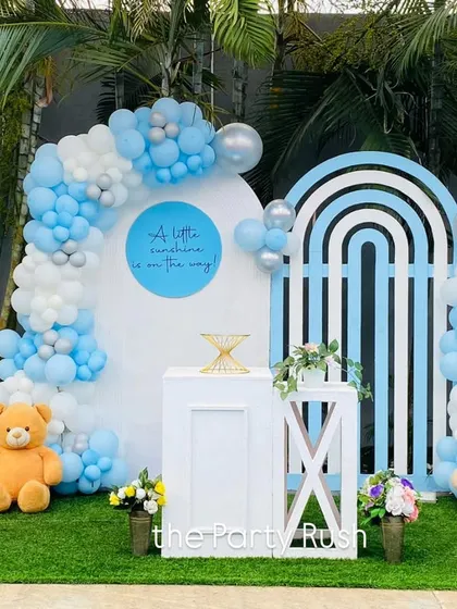 "A little sunshine is on the way." This charming blue and white baby shower theme is perfect for welcoming a baby boy. The setup includes modern arched backdrops, cute teddy bears, and soft balloon clouds.