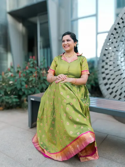 A lovely portrait of a woman in a unique green traditional dress, seated on a bench in a modern, urban setting.
