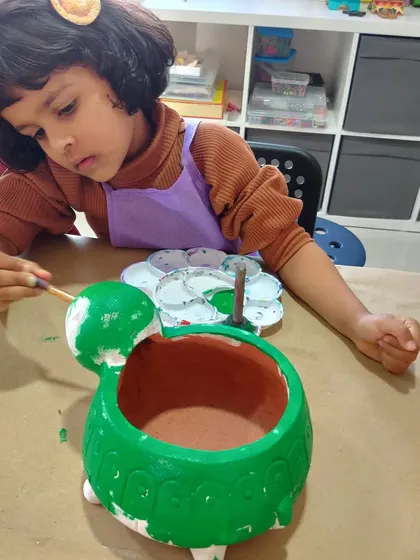This little artist is adding green paint to her turtle planter, fully engaged in the creative process.