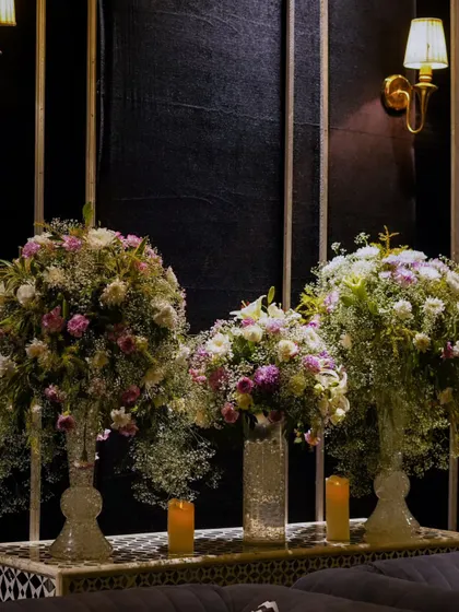A trio of stunning floral arrangements in glass vases, creating a major decorative statement against the dark, paneled wall.