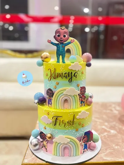 A cheerful and colorful two-tier Cocomelon cake, perfect for a first birthday. This tall cake features the beloved characters, rainbows, and a vibrant color palette, bringing the popular nursery rhyme show to life.