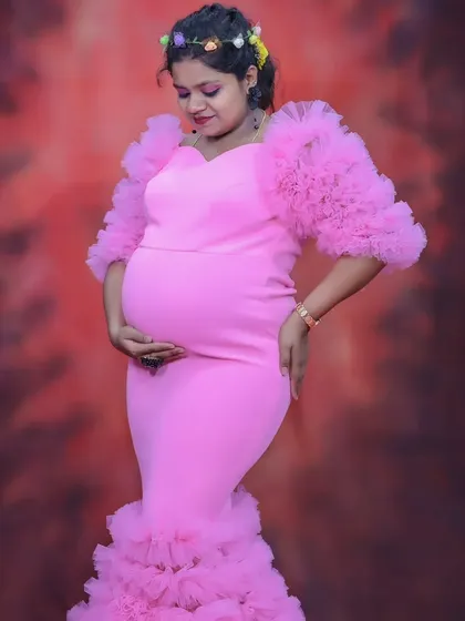 An elegant maternity portrait of a woman in a pink ruffled gown, gently cradling her baby bump.