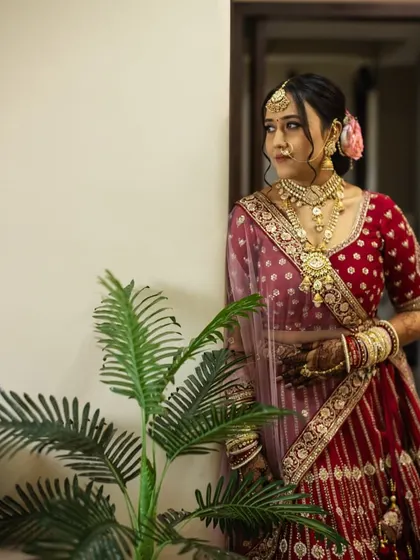 A candid shot of the bride in her stunning red lehenga. The makeup is soft and elegant, with a focus on creating a natural, radiant glow that looks beautiful in any light.