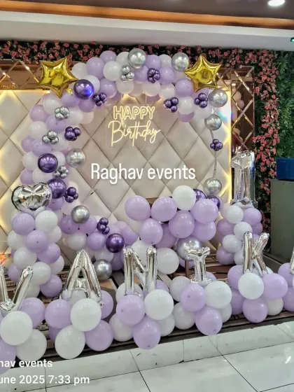 A grand birthday decoration for Vanika with a purple and white balloon arch against a quilted backdrop. The setup includes a neon sign and silver foil letters spelling out the name.