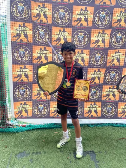 A proud champion from our U13 team holding his best player award and the winner's shield.