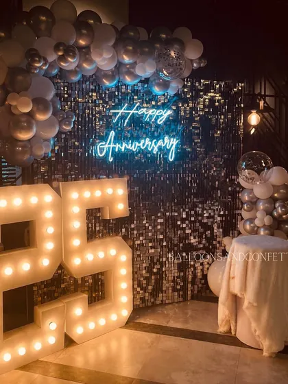 A wider shot of the 25th-anniversary decor. The marquee lights provide a warm glow that contrasts beautifully with the cool tones of the silver balloons and blue neon sign.