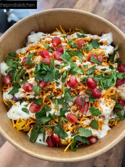 A close-up of my Samosa Chaat, a true taste of Delhi street food. I load it with crumbled samosa, cool yogurt, tangy chutneys, sev, and fresh pomegranate seeds for a perfect mix of sweet, spicy, and crunchy in every bite.