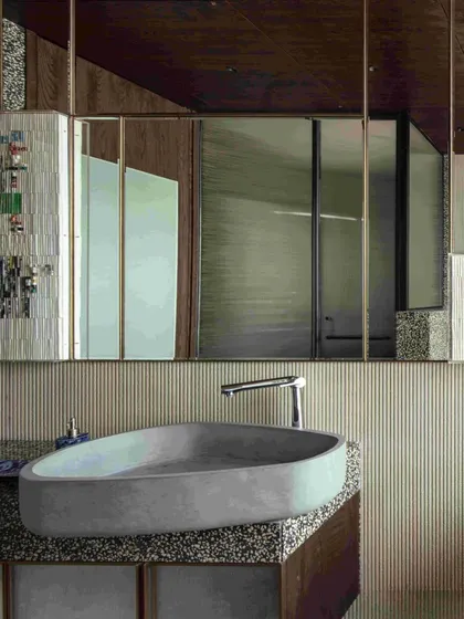 A close-up of the Gomaads concrete wash basin, set against a backdrop of fluted limestone and a large mirror. The design is a beautiful blend of raw and refined materials.