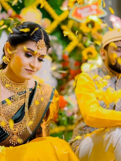 A serene moment from a Haldi ceremony, as the bride and groom are blessed with turmeric paste and flower petals. The floral backdrop adds to the beauty of the scene.