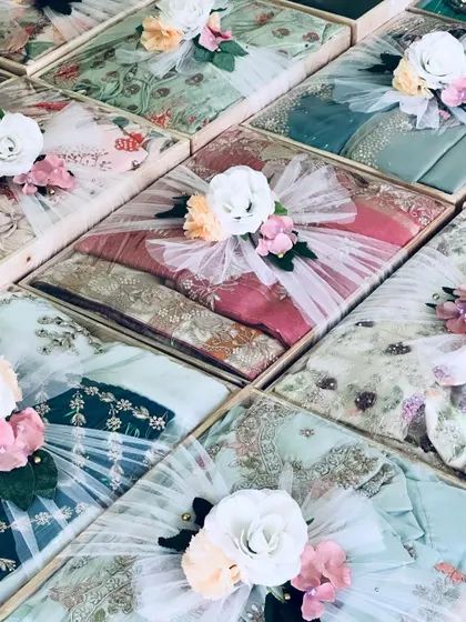 An array of pastel-themed trousseau gifts. The soft colors of the outfits and the delicate white floral arrangements create a cohesive and elegant display.