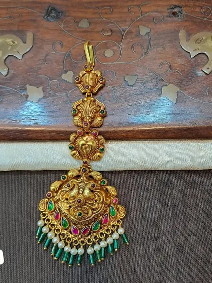 A beautiful peacock motif maang tikka made from 92.5 silver with gold plating. The green and pearl bead drops add a touch of elegance to this traditional piece.