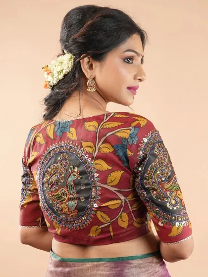 The back of this maroon blouse is a canvas for artistry, featuring a circular Kalamkari peacock motif. The intricate detailing on the back and sleeves makes it a stunning choice for any special occasion.