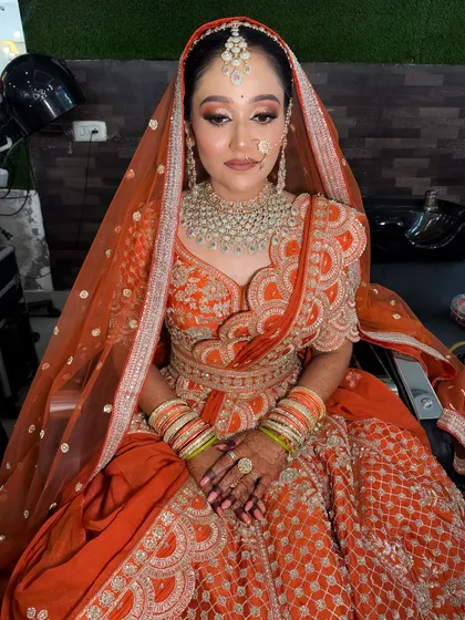 A stunning bride in a vibrant orange lehenga. The makeup is glamorous, with smokey eyes and a nude lip, perfectly balancing the bright color of her outfit.