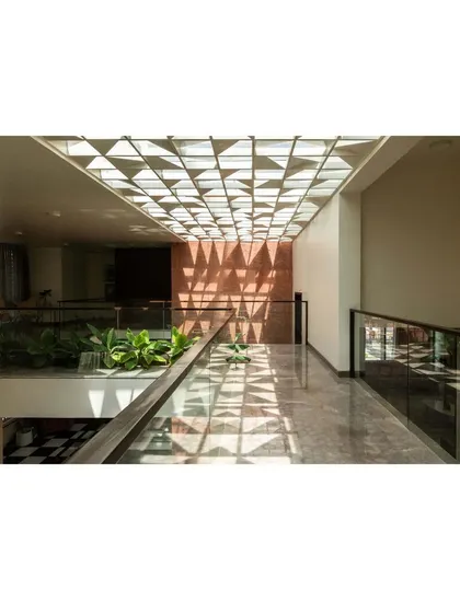 A bridge on the upper floor of the Notan Home offers a view down into the central courtyard. The geometric pattern of the skylight above is reflected in the shadows on the walls and floor, creating a dynamic and immersive spatial experience.