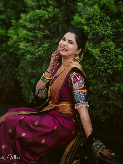 A joyful portrait of the bride, Shruti, seated and smiling, showcasing the detailed embroidery on her sleeve.