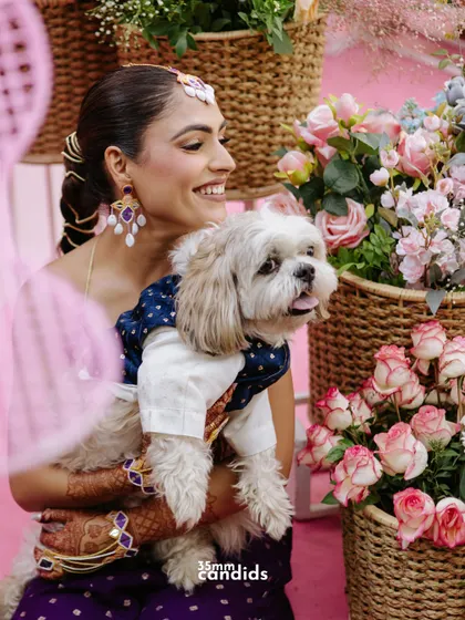The most important guest of honor! A heartwarming shot of the bride holding her beautifully dressed-up dog amidst the vibrant decor of her Mehendi ceremony.