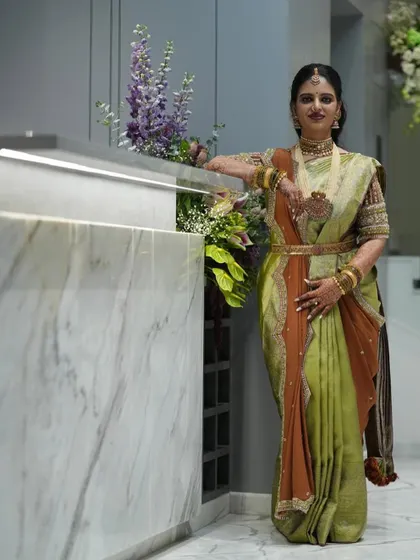 This client looks divine in her green and rust-colored saree. The custom-designed blouse with intricate embroidery adds a touch of elegance to her housewarming look.