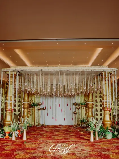 An elegant indoor mandap with golden pillars and strings of white jasmine. The design brings traditional grandeur into a classic ballroom setting for a timeless wedding ceremony.