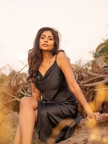 A seated portrait in a rustic, outdoor setting. The foreground and background elements frame the subject, creating depth and a sense of being immersed in nature.