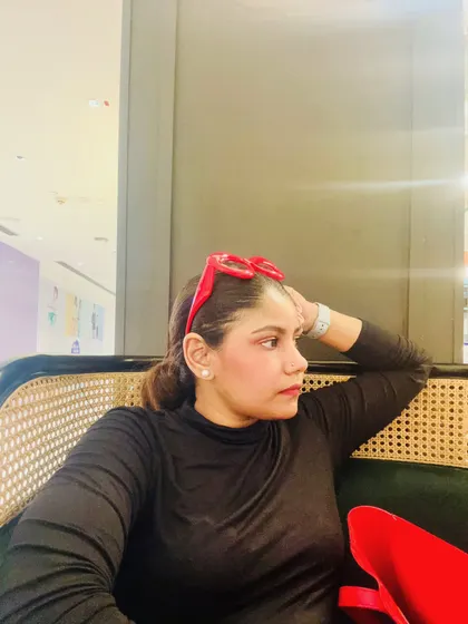 A candid shot while seated, wearing a simple black top and red heart-shaped glasses, showing a relaxed yet stylish moment.