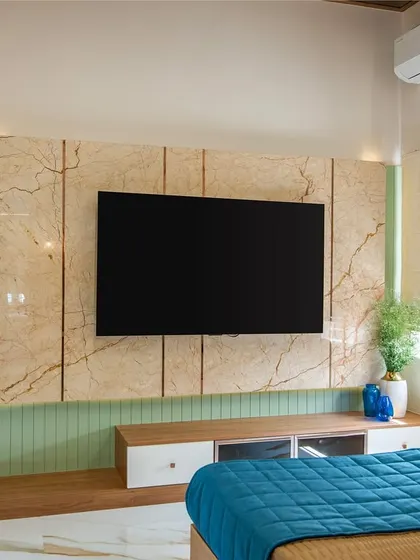 A view from the bed of the stylish TV wall. The combination of marble-look tiles, green fluted panels, and wooden shelves creates a multi-layered and visually interesting feature.