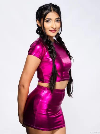 A fun and vibrant shot of a model in a metallic pink two-piece set with braided pigtails.
