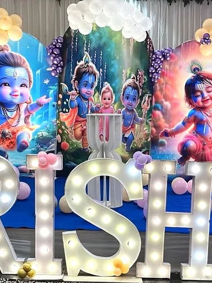 A divine Krishna-themed birthday decoration. This setup includes beautiful backdrops of Little Krishna, pastel balloon arches, and large marquee letters for the name.