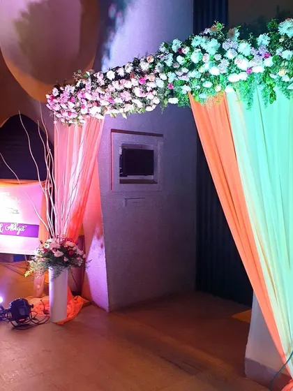 This simple yet elegant entrance features a floral header and soft, colorful drapes. A welcome sign and a vase with decorative branches are placed to the side, adding a modern touch.