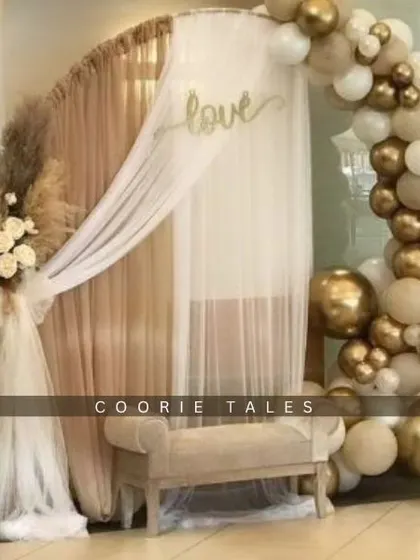 A dreamy boho setup for an intimate anniversary celebration. This design features a golden arch draped with sheer fabric, a neutral balloon garland, and dried florals, creating a warm and romantic atmosphere.